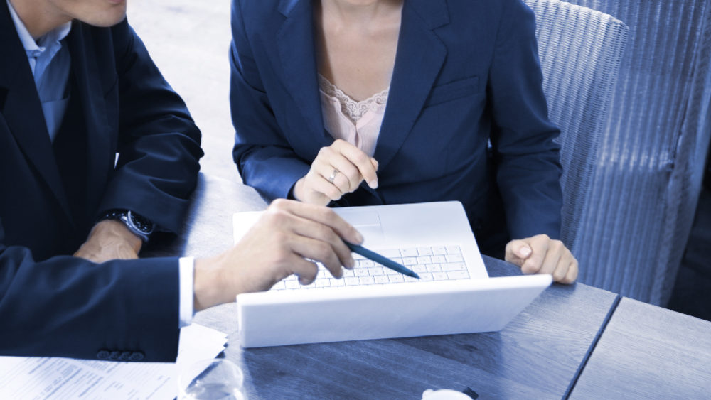 man pointing at a white laptop with a pen, women sitting next to him looking