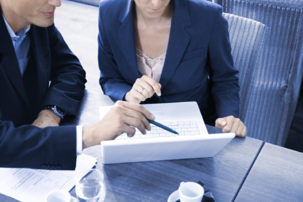 man pointing at a white laptop with a pen, women sitting next to him looking